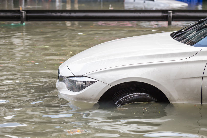 A white car is partially submerged in floodwater on a street, highlighting the importance of flood and water damage insurance claim adjusters.