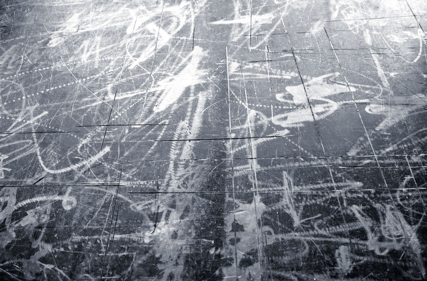 A black and white photo of a scratched, worn floor with extensive scuff marks and overlapping lines, possibly reflecting the aftermath of an incident that would be of interest to Building Vandalism Insurance Adjusters.